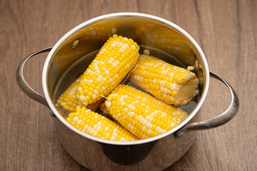 Four golden ears of corn are boiled in a silver pot filled with water. The vibrant kernels indicate freshness, making it a perfect side dish for any gathering