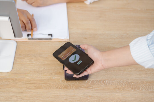 Person using smartphone for cashless transaction with credit card at point of sale terminal, emphasizing simplicity of contactless digital payment method in secure retail environment for consumer