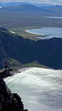 A hiker stands triumphantly on a rocky cliff, gazing at the stunning panorama of Norways dramatic coastline and lush valleys. Matind mountain hike Bleik Norway