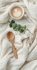 Creamy latte, wooden spoon, and eucalyptus sprig on a soft white blanket