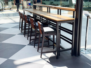 Tall wooden tables with high stools arranged by large windows in a public lounge. Representation of travel lifestyle, dining, and social atmosphere in modern hospitality spaces.