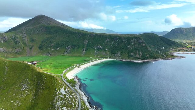 Breathtaking aerial perspective showcases Mannen mountain overlooking Haukland beach in Lofoten, Norway. Clear turquoise waters kiss the sandy shore, surrounded by lush green terrain.