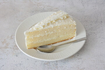 Slice of coconut cake on a white plate with a spoon
