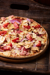 Pizza with ham, salami, cherry tomatoes and mozzarella cheese. Rustic wooden background. Soft focus. Close up.	