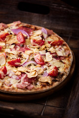 Pizza with ham, salami, cherry tomatoes and mozzarella cheese. Rustic wooden background. Soft focus. Close up.	
