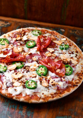 Pizza with salami, mozzarella cheese and jalapeno pepper. Wooden background. Soft focus.	