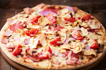 Pizza with ham, salami, cherry tomatoes and mozzarella cheese. Rustic wooden background. Soft focus. Close up.	