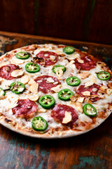 Pizza with salami, mozzarella cheese and jalapeno pepper. Wooden background. Soft focus. Copy space.	