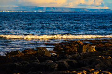 Coastal Waves with Reykjavik City and Mountains in the Background at Sunset, Iceland