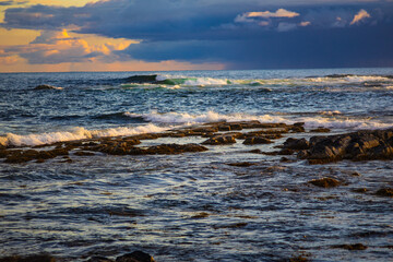Ocean Waves Crashing on Rocky Shore under Dramatic Sunset Clouds