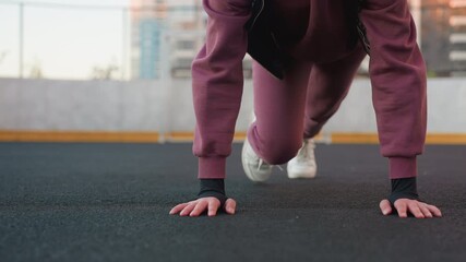 Hoodie wearing athlete doing foot crawl exercise on urban sports court floor with hands pressing ground and legs moving simultaneously for core stability strength mobility during outdoor city workout