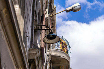 Old rusty lamp on a tenement facade next to a decorative balcony with wrought iron railing