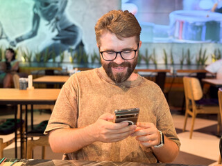 Man sitting in a lounge chair while looking at his phone. Technology, communication, and leisure illustrated through travel waiting moments and everyday digital habits.