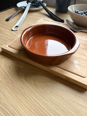 A round brown ceramic baking dish stands on a wooden cutting board in the kitchen. Cookware, home cooking, and culinary preparation reflect lifestyle, culture, and household traditions.