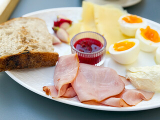 A breakfast plate with ham, cheese, eggs, bread, and jam served with tea. Nutrition, lifestyle, and dining culture illustrate morning meal, tradition, and balanced food choices.