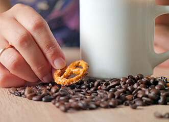 Hand placing pretzel by coffee - Hand carefully places a golden-brown, salt-crusted pretzel on a table next to a white coffee mug filled with a hot drink