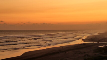 Fototapeta premium Scenic tropical beach sunset with golden sky, ocean waves and silhouettes of people along the coastline