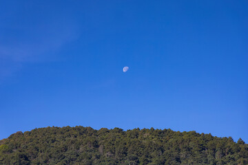 The moon in a blue sky over the mountain.