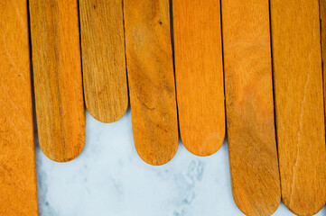 Top view of aligned wooden popsicle sticks on white marble background, showing natural grain and smooth texture.