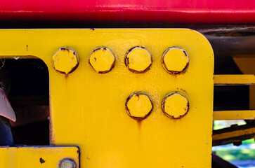 Close-up of six large rusty bolts on a yellow flange, with red metal above.
