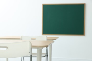 Blank green chalkboard, desks and chairs in classroom, closeup