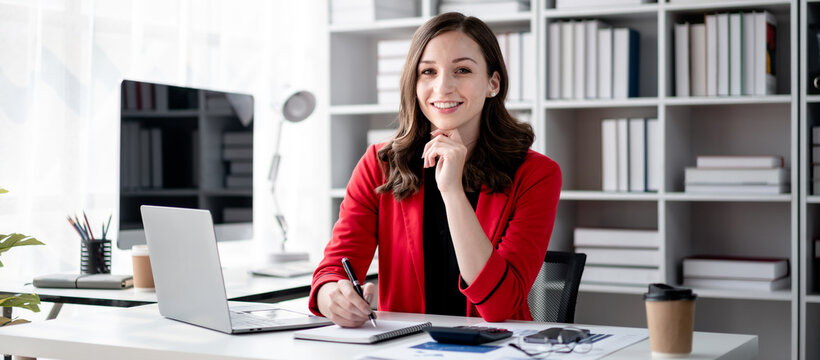 Business Woman Writing Notes at Desk with Laptop in Office Setting | Financial Planning and Investment Strategies for Growth | Adult Professional