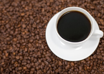 Top view, White espresso cup on saucer over coffee bean background