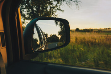 View on the road in the side mirror in front of the meadow at sunset. Beautiful view from the car to the field. Travel concept, adventures on the holidays. © ksana_uk