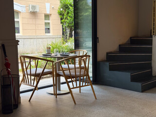 A wooden dining table with chairs and glassware stands by a window in a cafe. Hospitality, lifestyle, and leisure reflect urban dining culture and social atmosphere.