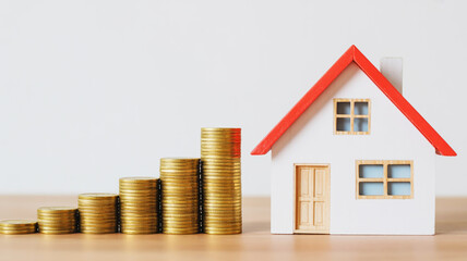 Stacks of gold coins increasing in height next to a miniature house with a red roof money growth