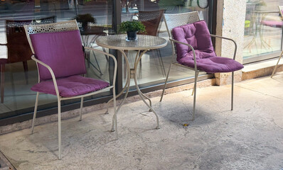 Outdoor cafe seating with purple cushions. Relaxation, leisure, and social interaction in a cozy street cafe setting.