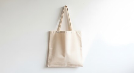 Plain beige canvas tote bag hanging on a white wall