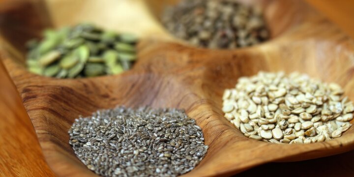 An eye-level close-up of a wooden bowl filled with an assortment of seeds.
