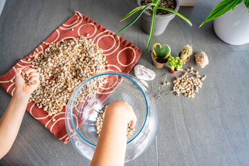 Close-up of child hands pouring stones into a glass container while preparing drainage for a florarium or closed ecosystem. Tactile learning, mindful creativity and eco-friendly crafting.