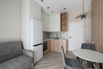 modern, compact kitchen-living area. The design features white cabinetry, a grey sofa, a white...