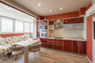 modern kitchen with red cabinets, a light wood floor, dining table and a sofa with a view outside