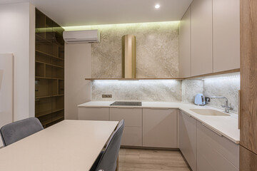 Modern kitchen with marble backsplash, sleek cabinets, and a dining table with grey chairs. Overhead lighting adds a warm ambiance