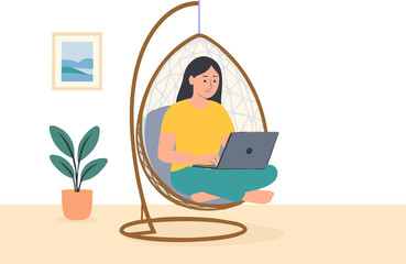 young woman sitting on a modern hanging egg chair  with cushions, indoors, comfortably working on a laptop