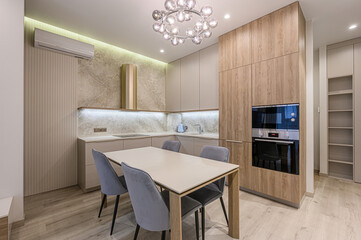 modern kitchen with light wood cabinets, a marble backsplash, a dining table with four chairs, and a stylish chandelier