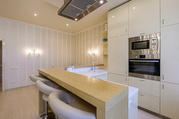 modern kitchen with an island, bar stools, stainless steel appliances, and beige cabinets, under lit by recessed ceiling lights