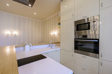 modern kitchen with cream cabinets, stainless steel appliances, a white countertop, and striped wallpaper. The room is well-lit with modern fixtures