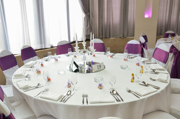 A round table for guests at a wedding celebration with purple details ready for fourteen people and marked with the number nineteen