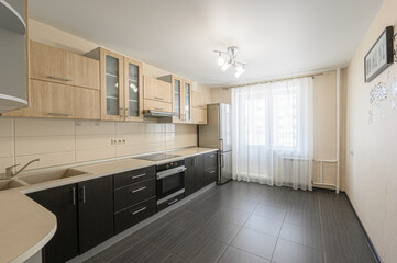 bright, modern kitchen with wood cabinets, dark countertops, stainless steel appliances, and grey tile flooring. Large window with sheer curtains