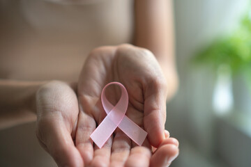 Female hand presenting pink satin ribbon, symbolizing breast cancer awareness, self-diagnosis...
