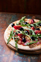 Pizza with salami, tomatoes, mozzarella cheese, black olives and arugula. Rustic wooden background. Soft focus.	