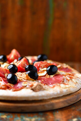 Pizza with ham, salami, tomatoes and mozzarella cheese. Rustic wooden background. Soft focus. Close up.	
