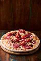 Pizza with salami, tomatoes and mozzarella cheese. Rustic wooden background. Soft focus. Copy space.	