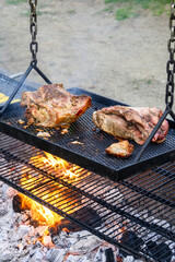 Cooked pork roast staying warm on a rack hanging higher above the grill, dripping grease cause fire to flame up, as part of luau dinner preparations
