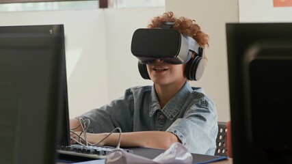 Cute schoolboy with virtual reality headset sitting by desk in front of computer monitor at lesson of programming, watching 3d video and commenting immersive experience - Powered by Adobe