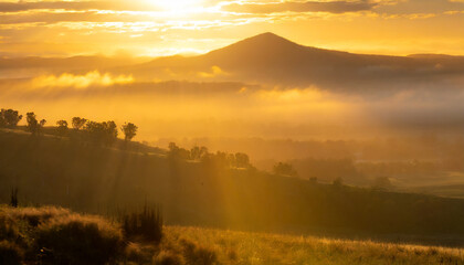 Golden sunrise over mountain landscape, sunlight rays streaming through morning mist, serene valley, silhouettes of trees, atmospheric nature view for relaxation, travel, backgrounds, calm mood